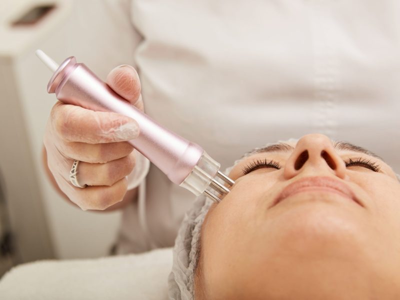 Close up of female cosmetologist hand using professional lifting device while performing face rejuvenation procedure